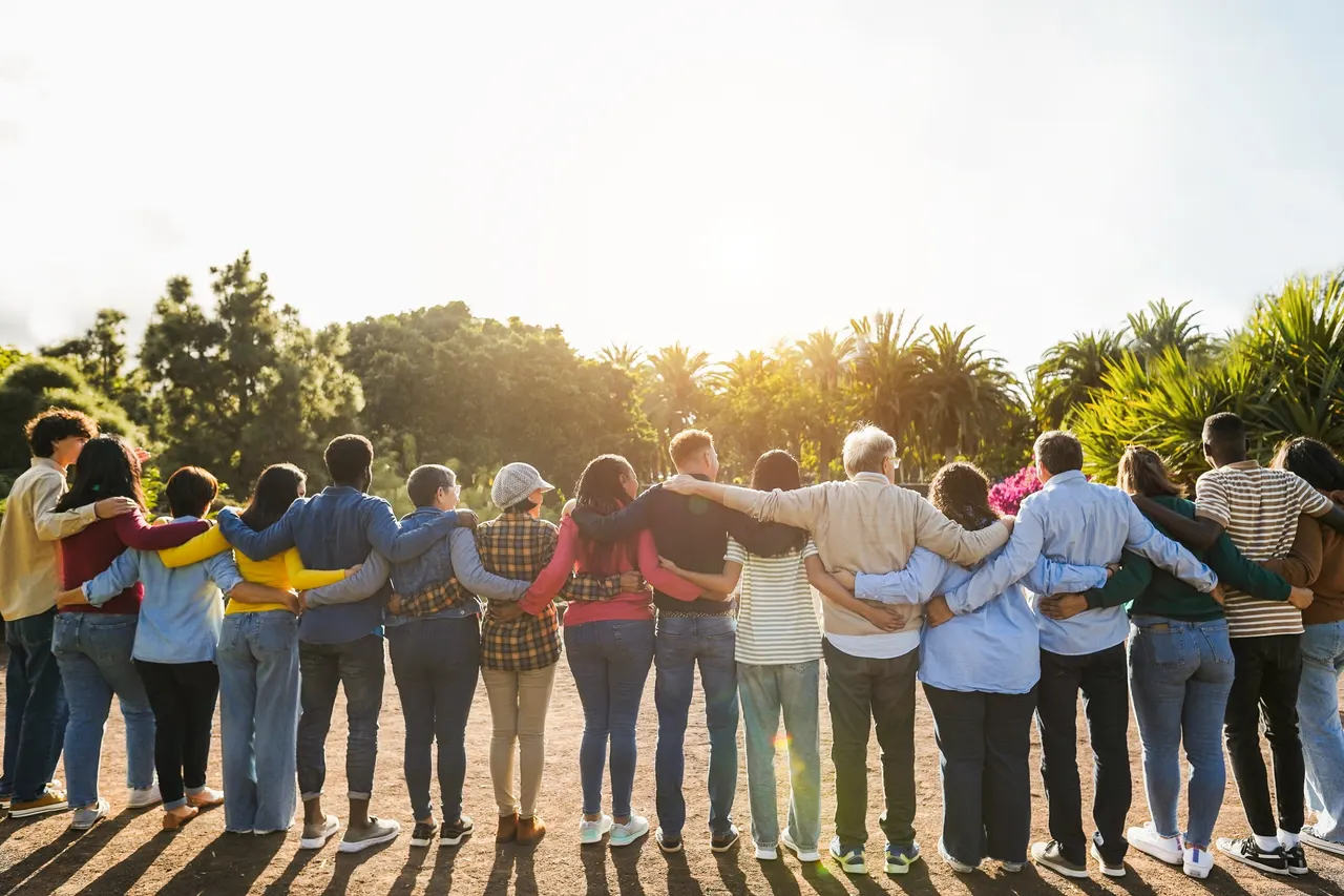 A diverse, multigenerational group standing arm in arm, facing the sunset together